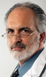 Close-up portrait of a doctor wearing glasses and a white lab coat. He is looking at the camera with a serious expression. Vertical format.